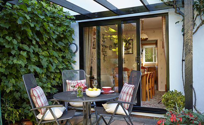 Jet Black aluminium patio doors sliding open to outside patio with black pergola and greenery