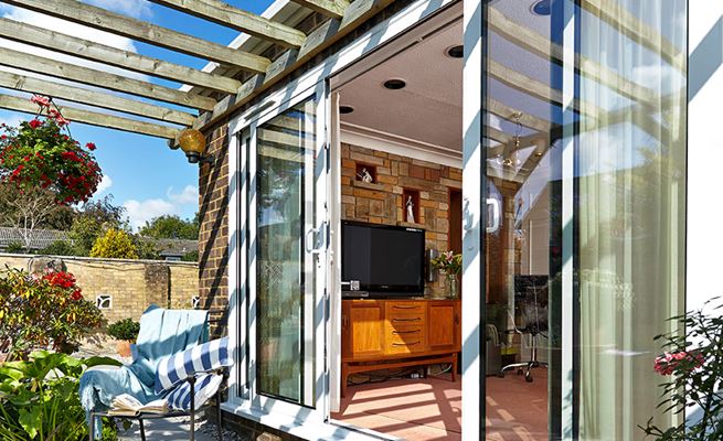 White aluminium patio doors with white handles sliding open to outside patio with timber pergola